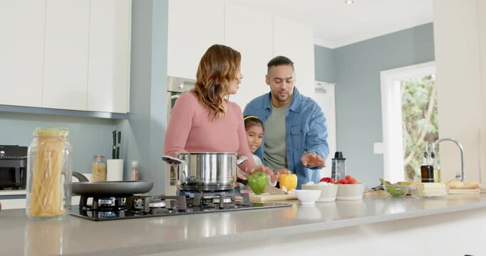 Diverse family assembling salad in kitchen as mother slicing pepper triggers father dicing peppers