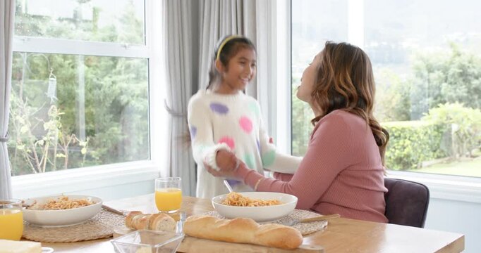 Mother and daughter greeting with tap, hug, clinking glasses and eating pasta at dining table