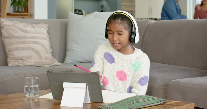 Receiving call, Asian schoolchild launching tablet call jotting notes for homework on sofa