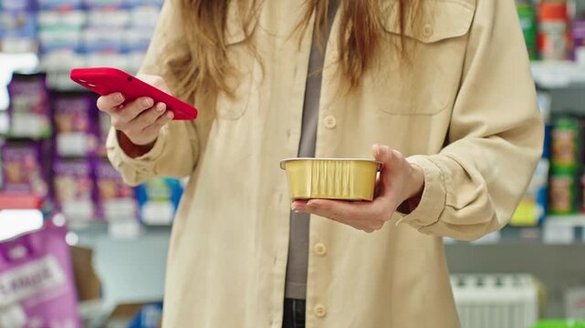 Woman scanning pet food product with smartphone in store, checking information before purchase, mobile assisted shopping in pet shop or supermarket, smart consumer behavior