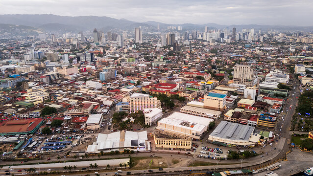 Cebu City, Philippines, Aerial Sunset Panorama of Coastal Urban Landscape, featuring the busy port area, dense urban skyline, and distant mountains under a golden sky