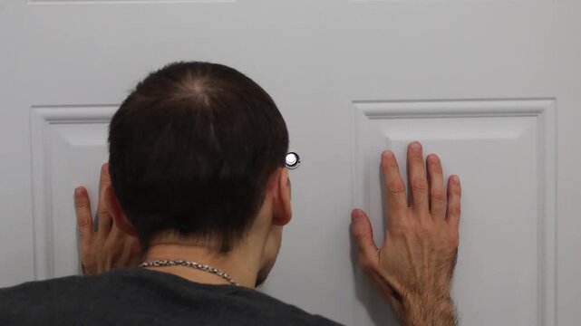 Man looking through door peephole with hands on surface checking outside situation