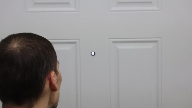 Man slightly stepping back from door after checking peephole indoors
