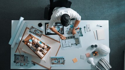 Top view of project manager writing house idea on sticky notes while looking plan at tablet. Aerial...