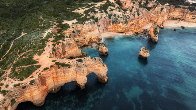 Aerial view of rugged golden cliffs meeting the turquoise sea at Praia da Marinha, forming natural arches and stacks, Portimao, Faro, Portugal.