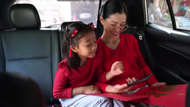 Thai Mother and Daughter Using Smartphone to Translate Chinese New Year Red Envelopes in Car, Handheld Shot of Authentic Family Celebration in Asia.