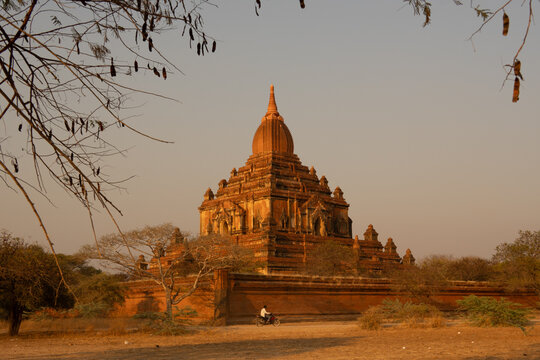 View of a majestic, sun-kissed temple rising from the arid landscape, its ancient brickwork glowing warmly against the pale sky, Old Bagan, Mandalay Region, Myanmar.