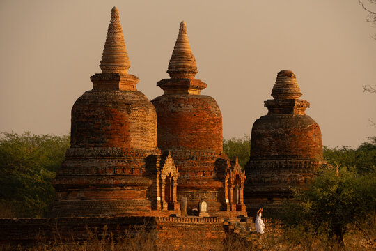 View of ancient brick pagodas rising from the earth, bathed in the warm glow of the setting sun, a spiritual journey through time, Old Bagan, Mandalay Region, Myanmar.