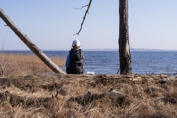 Boy resting on a fallen tree near the lake, eating snack and enjoying quiet nature. Concept of childhood, outdoor relaxation and simple life.