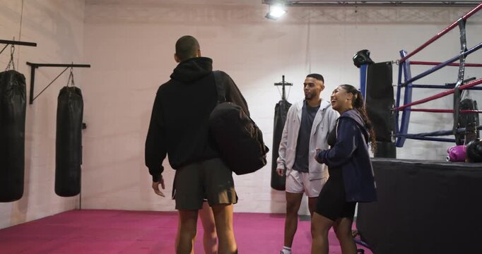 Diverse friends greeting newcomer after arriving carrying duffel bag onto pink mats at boxing ring
