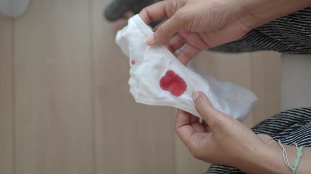 Woman's hands holding white underwear with red blood stain, symbolizing menstruation, period, or vaginal bleeding issues close up motion footage