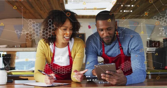 Vertical video: Showing orders on tablet, two partners tapping and writing at counter in red aprons