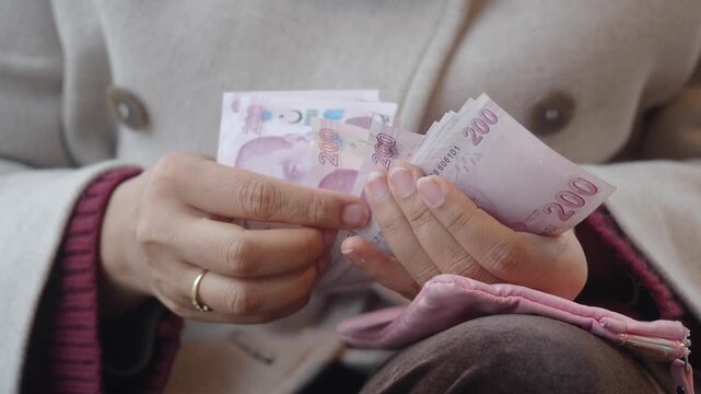 Woman hands counting stack of two hundred turkish lira banknotes while sitting outdoors on bench in winter