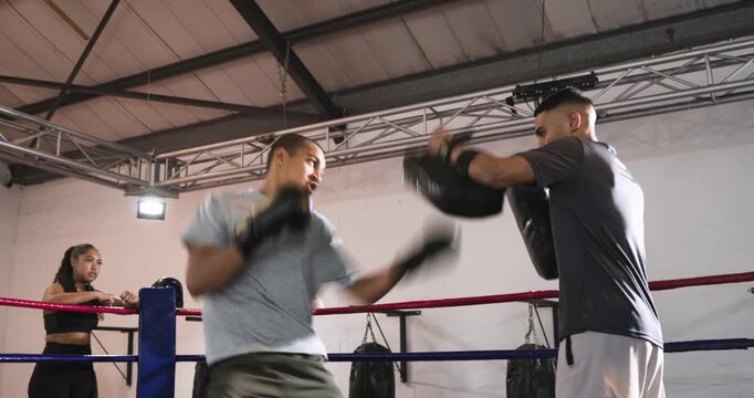 African American boxer trainee and coach trading combos after pad lowering in ring for training