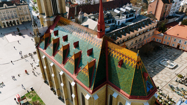 Aerial view of the vibrant, patterned roof of the Name of Mary Church stands out against the stark shadows of the surrounding square, Sad, Vojvodina, Serbia.