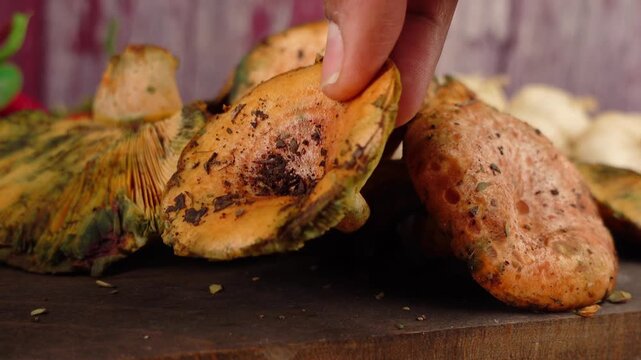 Close up of hand picking up fresh saffron milk cap mushroom from wooden table