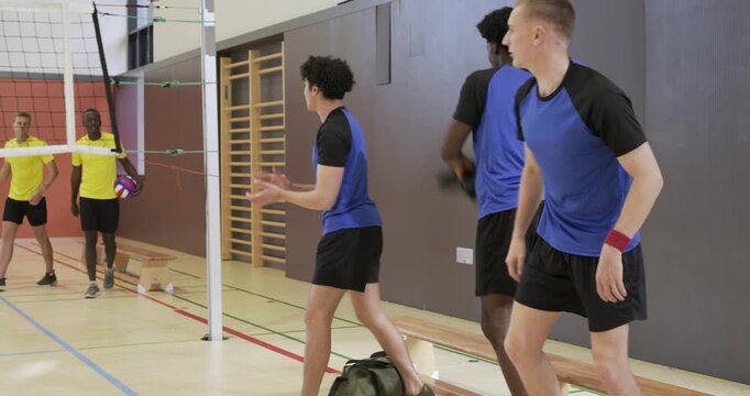 Three male blue team after exchange standing crossing net greeting opponents preparing play at gym