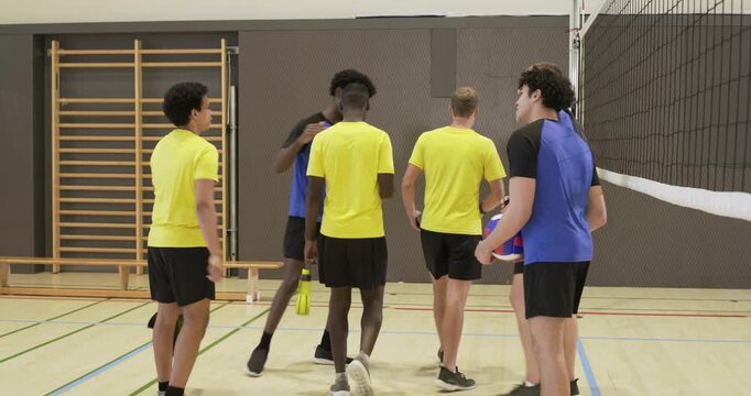 Six male players meeting at net in school gym after match, greeting, passing volleyball and bottles