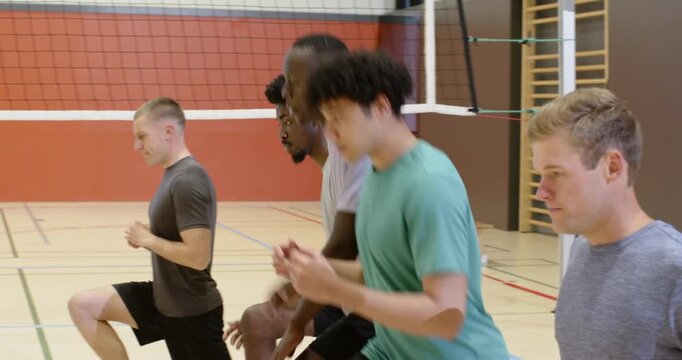 Diverse male teammates assembling in gym along volleyball net, marching and jogging, warming up
