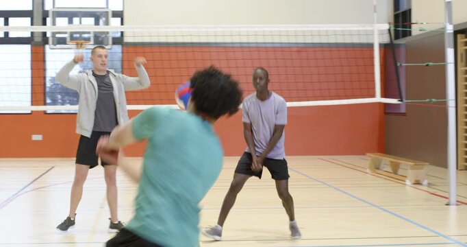 Male teammates practicing in gym, man in purple tee following teammate pass receiving volleyball