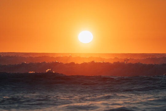 View of the sun ablaze in a fiery sky, casting an orange glow across the rippling waves of the ocean, a serene moment captured, Cabeco da Arveloa, Portugal.