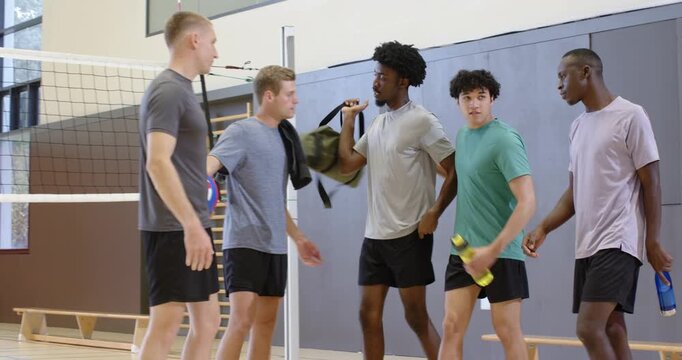 Diverse male teammates grabbing volleyball and duffel, huddling at school gym preparing match