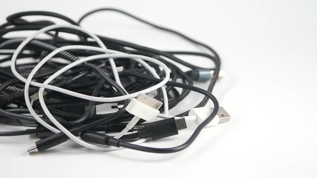 A jumbled pile of black and white charging cables and data cords on a white background, demonstrating electronic waste and tangled connections