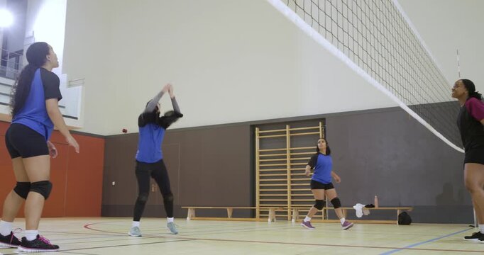 Four women volleyball players in knee pads reacting to ball going over net, practicing forearm pass