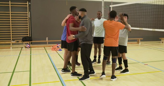 Diverse male volleyball team responding to coach signal, converging for pep talk at gym net