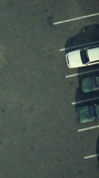Vehicles are parked in rows in a parking lot. The view is from above, showing the layout of the cars and the surface of the lot. There is a patch of unclear area in the lot.