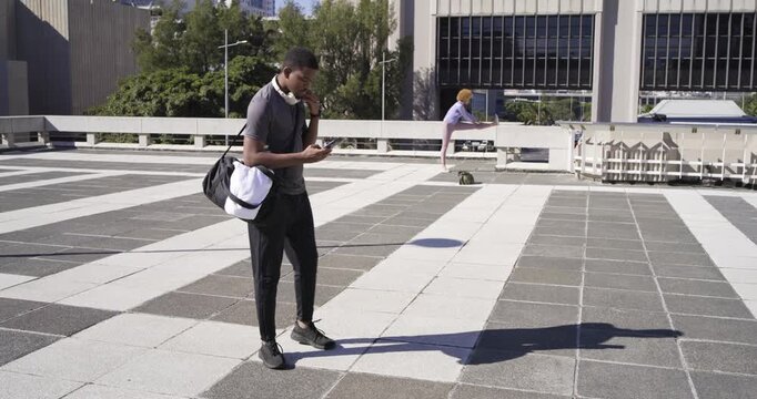 African American man, woman on roof, man checking phone, using headset, woman picking bag, skating