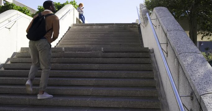 2 at stairs African American man holding basketball climbing toward landing as woman checking cell
