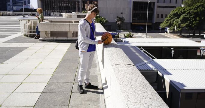 Adult male holding ball walking rooftop pausing at railing placing ball checking phone, copy space