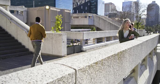 Woman walking urban stairs, stopping at concrete ledge after phone ringing, holding cup, copy space