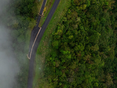 Aerial view of a winding road cutting through the dense, vibrant green forest, partially obscured by ethereal, drifting fog., Cinchona, Alajuela Province, Costa Rica.