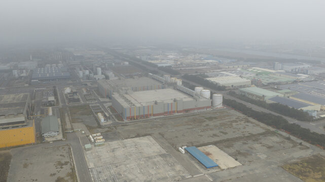 Aerial view of industrial buildings and storage tanks shrouded in a dense, hazy atmosphere, casting a muted palette over the landscape, Changhua County, Taiwan.