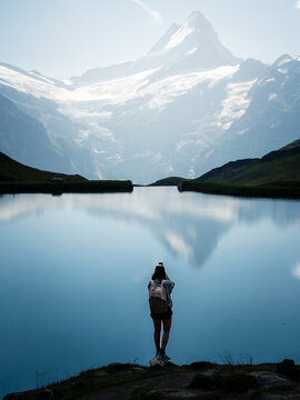 Aerial view of a serene lake mirroring the majestic, snow-capped Eiger mountain as a lone traveler gazes in wonder, Grindelwald, Switzerland.