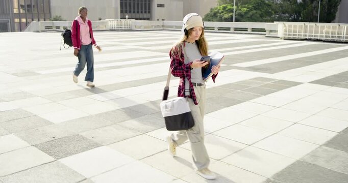 Diverse women walking across plaza, checking phone and holding notebooks, commuting past sculpture
