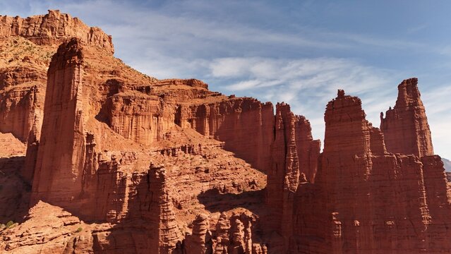 Aerial view of towering red rock formations pierce the sky, their rugged textures contrasting with the soft clouds above, landscape of canyons, Moab, Utah, United States.