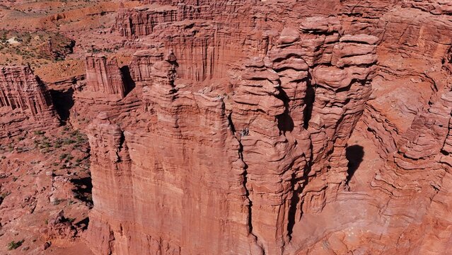 Aerial view of the Fisher Towers' towering red sandstone cliffs under a vast blue sky, a desert landscape sculpted by time, Moab, Utah, United States.
