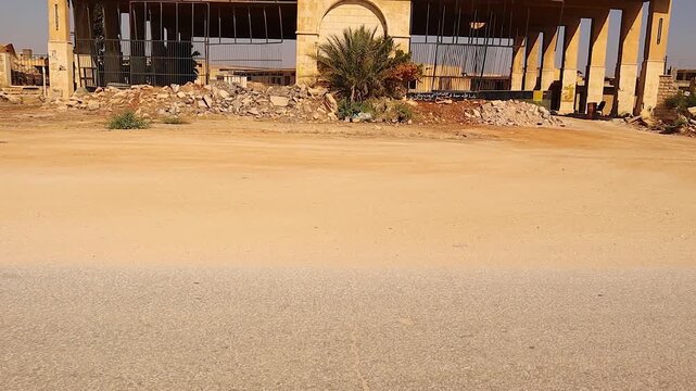 Entrance of an abandoned military base near the civilian prison in Aleppo, Syria. Gate and surrounding base buildings are bomb-damaged, showing war aftermath and infrastructure destruction for news
