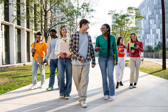 A diverse group of students is happily walking together on their university campus today