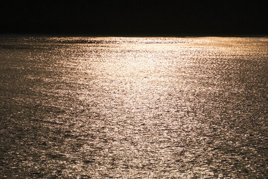 Golden Sunset Reflecting on Calm Sea with Forested Hill Silhouette