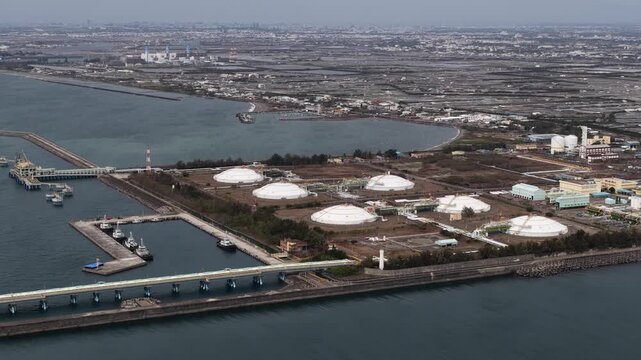 High angle aerial perspective of a liquefied natural gas terminal, showing massive storage tanks and an intricate network of pipelines essential for energy distribution and processing