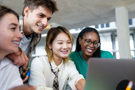 A diverse group of individuals is collaborating enthusiastically on a laptop in a modern workspace