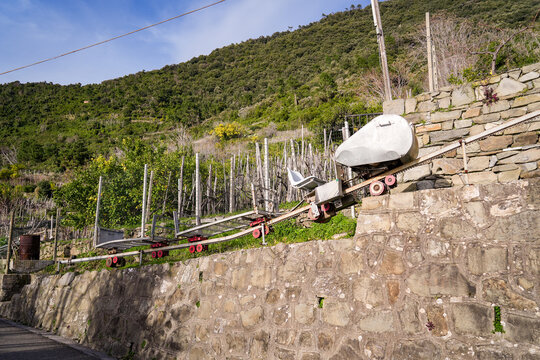 View of a monorail transport system clinging to a stone wall, with lush green hills rising behind in Manarola, Liguria, Italy.