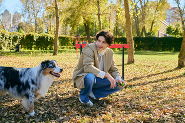 Fototapeta premium Young man enjoys a sunny spring day with his Australian Shepherd in the park