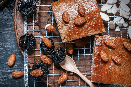 Pieces of banana cake topped with roasted almonds and dried prunes on wire rack.