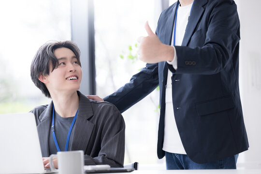 会社の仕事中に上司に励まされる新卒などの新入社員の爽やかなイメージ　その調子！仕事頑張ってね！OJTで先輩に指導を受ける若手社員の成長と教育のビジネスシーン
