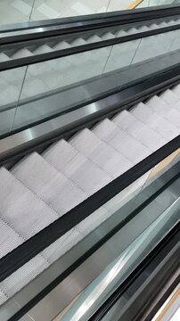Metal escalator steps in motion, closeup of empty stainless steps with glass balustrade, sleek handrail lines and repetitive treads. No people